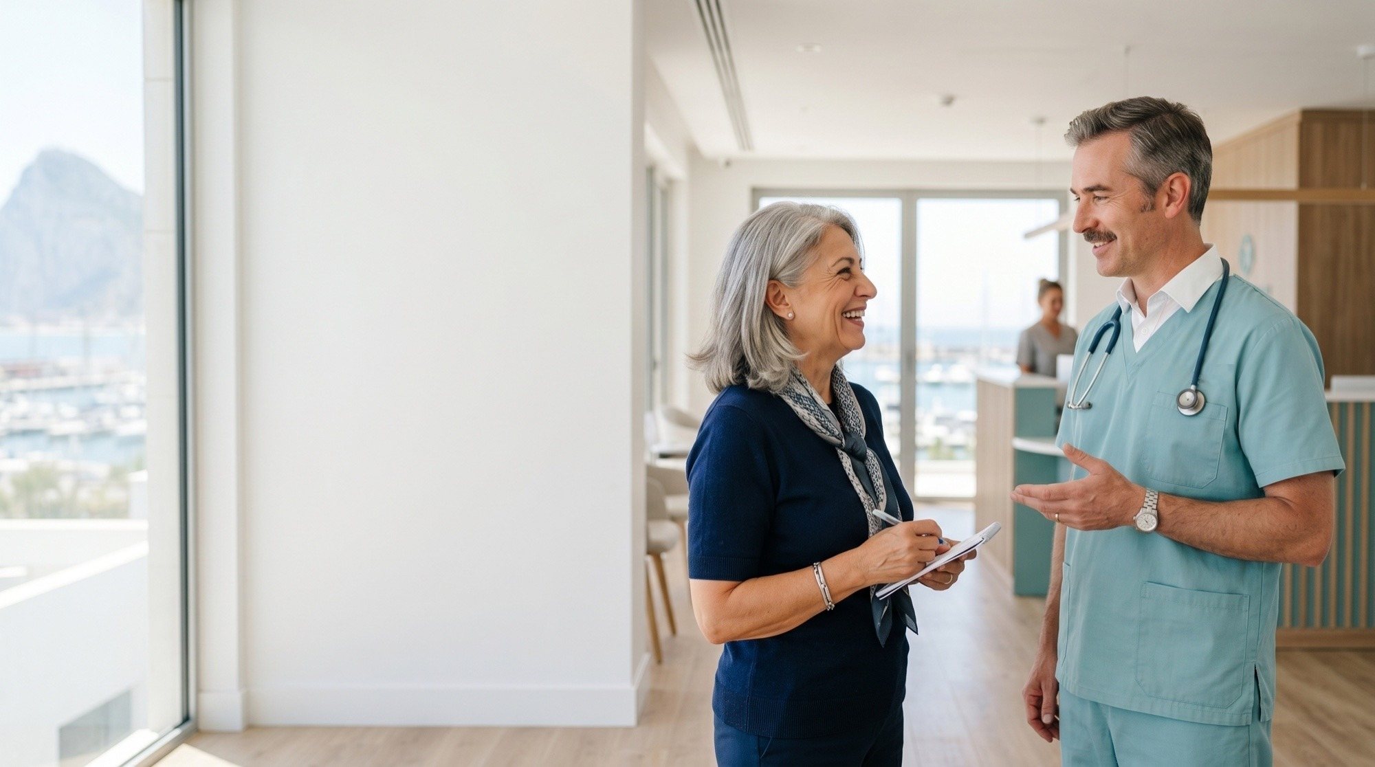A GibMed consultant in scrubs speaking with a smiling patient in a bright clinic overlooking Gibraltar's marina